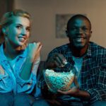 Man and woman watching TV and eating popcorn on a couch