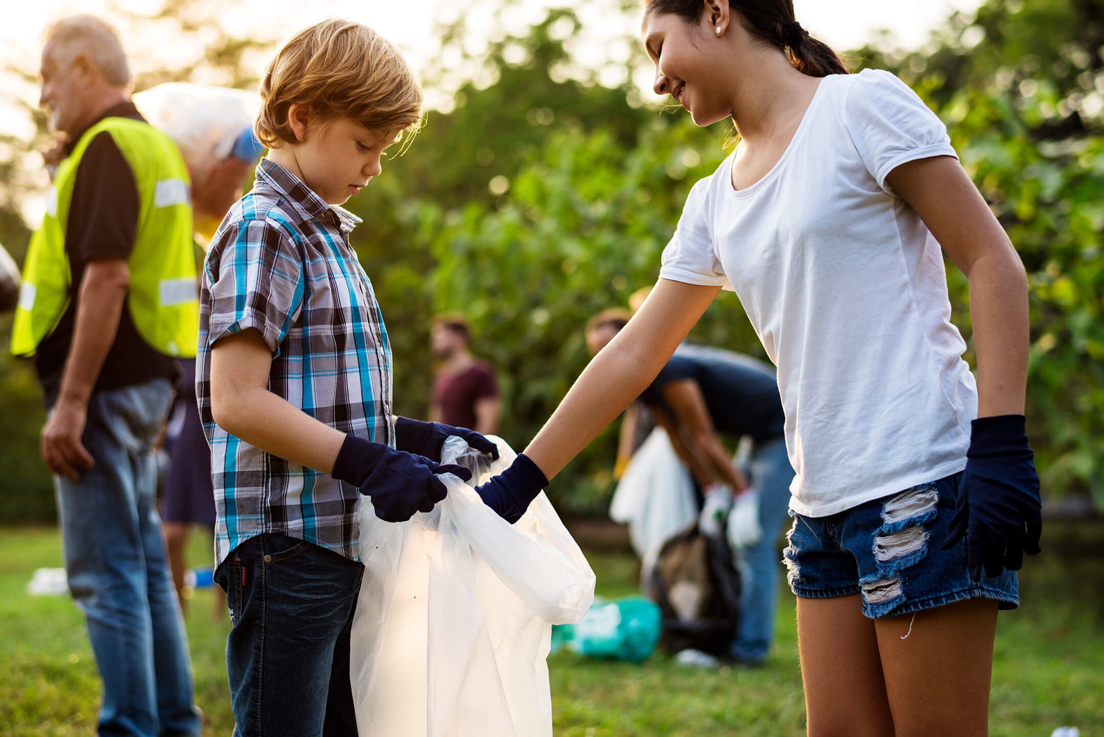 A girl putting trash into a trash bag being held by a boy