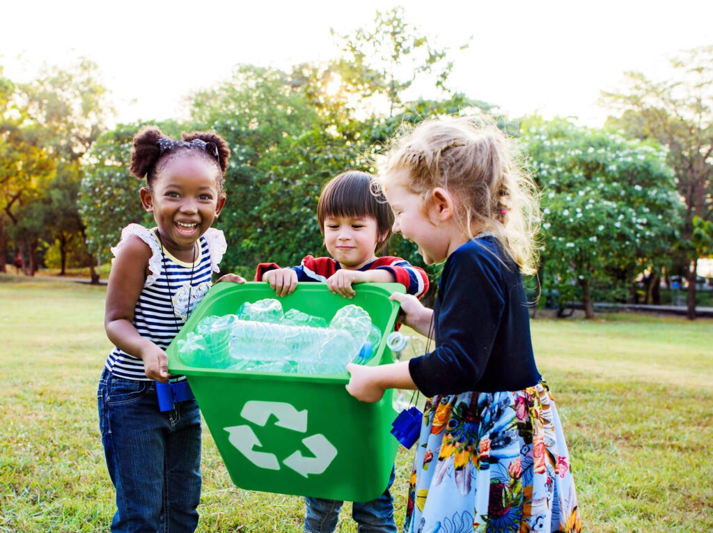 Three kids holding a recycling bin and smiling